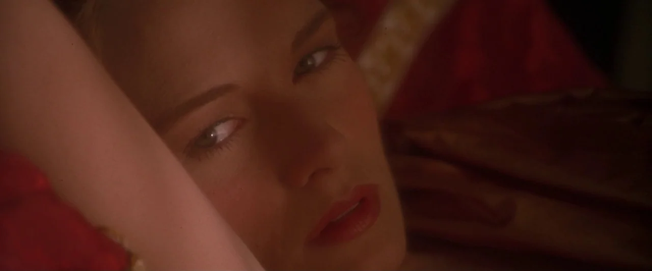 Dangerous Beauty (1998) movie still: closeup — A dark, dimly lit space features a woman resting on a soft surface. She lies back while gazing…