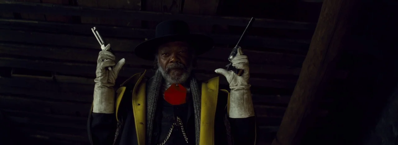 The Hateful Eight (2015) movie still: medium — A dark, cramped wooden attic interior features exposed rafters and shadows. An older man stands…