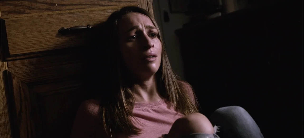 Hellbreeder (2004) movie still: closeup — A dimly lit room with dark wood paneling provides a stark background for a subject. A woman in a pink…