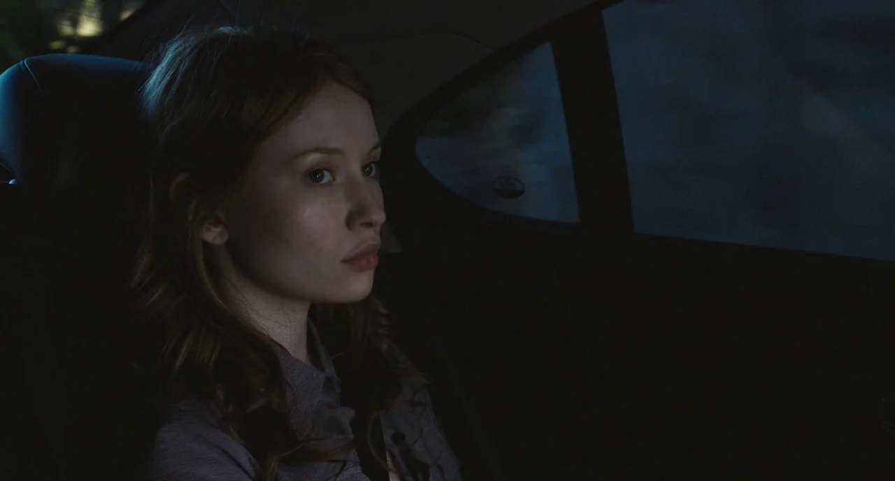 Sleeping Beauty (2011) movie still: medium — A dark vehicle backseat with a window displaying passing blurred lights at night. A young woman sits in…