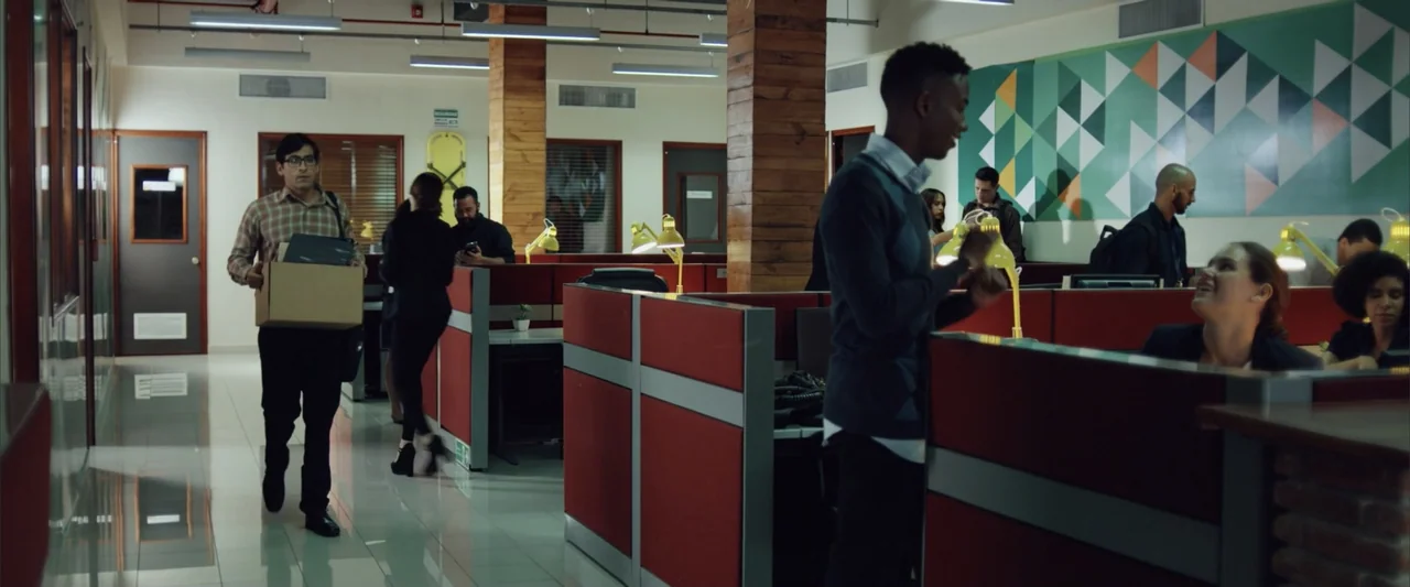 La Musiquita por Dentro (2019) movie still: medium — A modern open plan office features red partitions and white walls with geometric wall art. A…