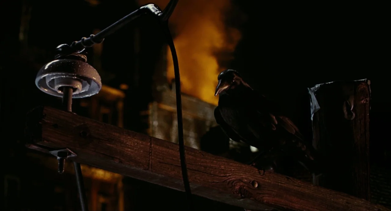 The Crow (1994) movie still: medium — A dark wooden utility pole sits against a black night sky backdrop. A black bird perches on the pole near a…