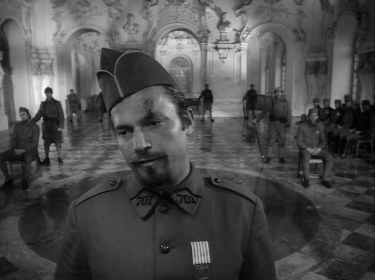 Paths of Glory (1957) movie still: medium — A man in a military uniform stands in the center of an ornate, vast ballroom. Numerous soldiers sit or…