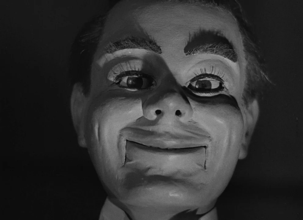 Dead of Night (1945) movie still: closeup — A close-up view of a ventriloquist dummy head against a pitch black background. The puppet displays a…