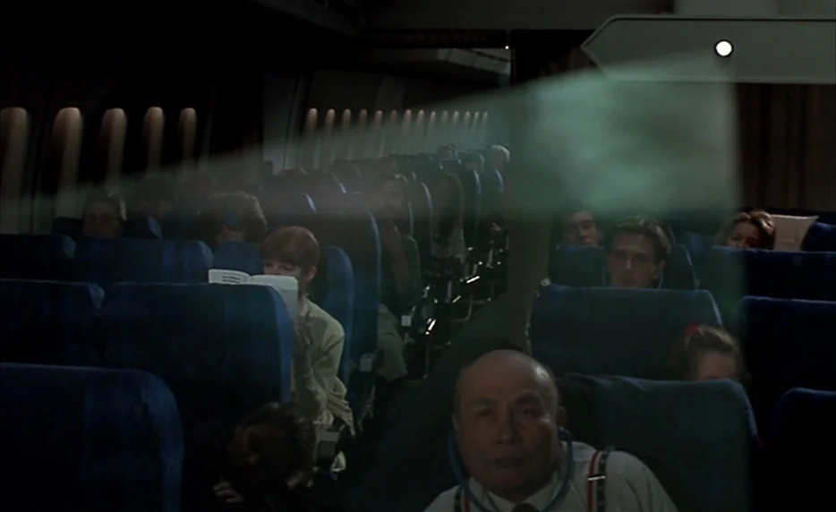 I Want To Go Home (1989) movie still: wide — An airplane cabin interior at night features rows of blue seats occupied by passengers. A light beam…