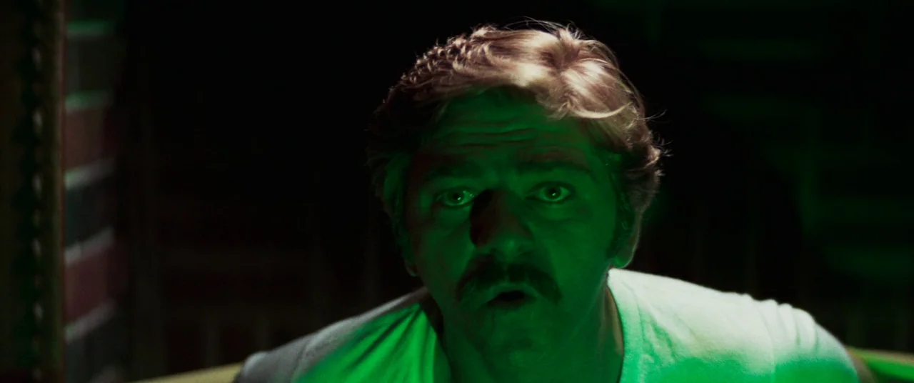 Death Game (1977) movie still: closeup — A man stands in a dark environment illuminated by a concentrated green light source. He looks toward the…