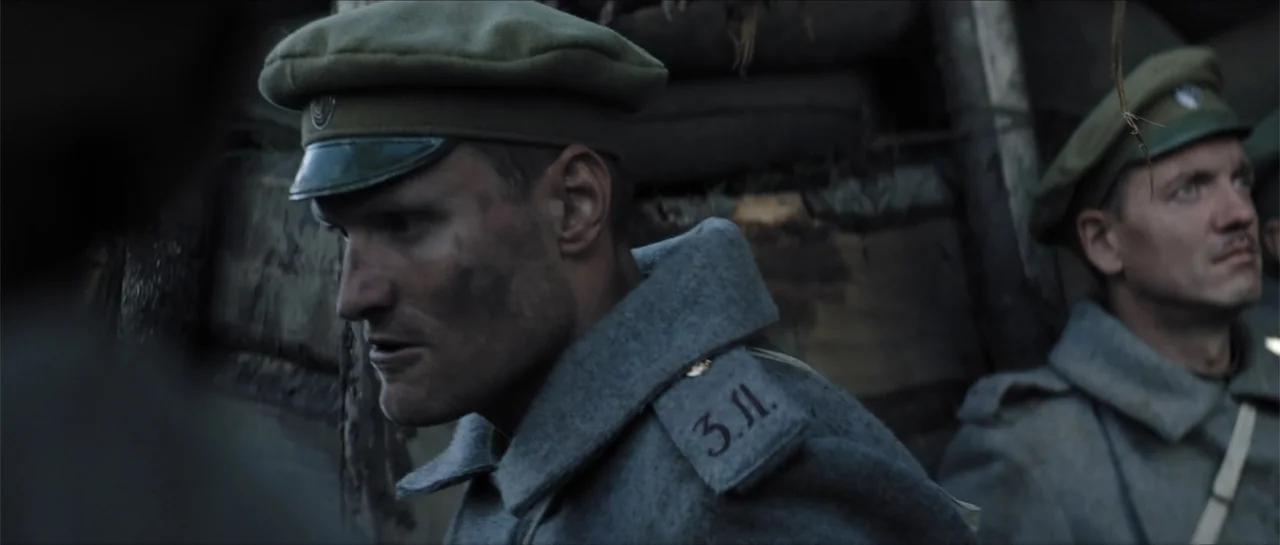 The Rifleman (2019) movie still: medium — A muddy, timber-lined military trench from the early twentieth century. Two soldiers in grey wool coats…