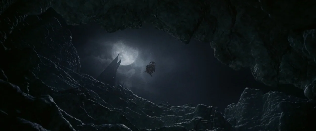 Harry Potter and the Chamber of Secrets (2002) movie still: establishing — A dark rocky cave opening frames a distant nighttime landscape under a…