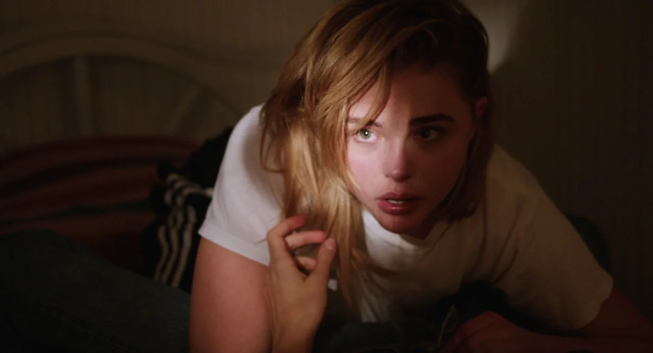 The Miseducation of Cameron Post (2018) movie still: closeup — A dimly lit room features a person reclining on a bed at night. The woman looks…