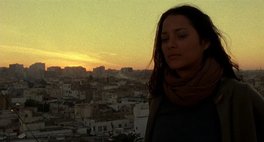 Furia (1999) movie still: medium — A rooftop overlooks a dense cityscape during a golden hour sunset. A woman stands in the foreground, facing away…