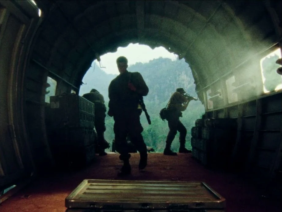 Da 5 Bloods (2020) movie still: fullbody — The interior of a military transport plane with corrugated metal walls and cargo boxes. Soldiers stand…