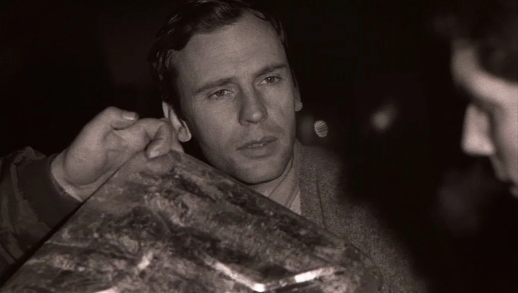Un Homme et Une Femme (1966) movie still: closeup — A man is in a darkened interior space. He holds a rectangular object towards an unseen person.