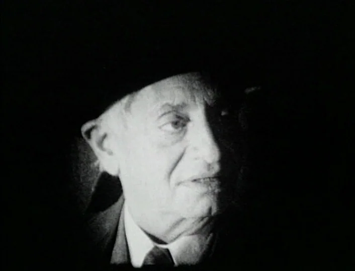 Cowards Bend The Knee (2003) movie still: closeup — An elderly man is framed against a solid black, featureless background. He looks slightly to the…