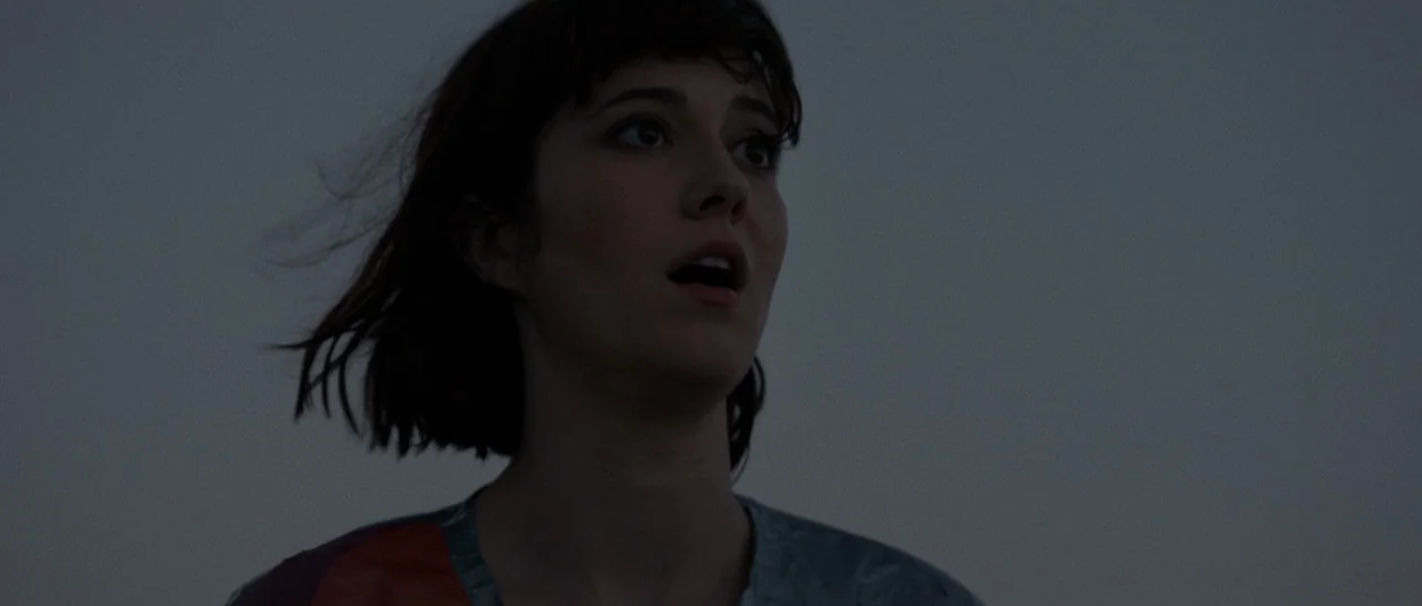 10 Cloverfield Lane (2016) movie still: closeup — An open outdoor area at blue hour with a clear, dark sky backdrop. A young woman with short brown…