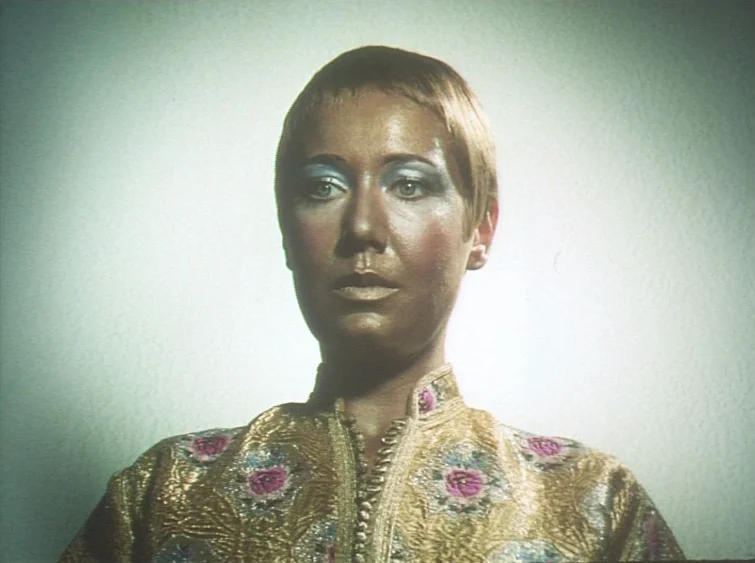 Hermitage (1968) movie still: closeup — A person stands against a featureless white wall in a sterile environment. A subject with gold-painted skin…