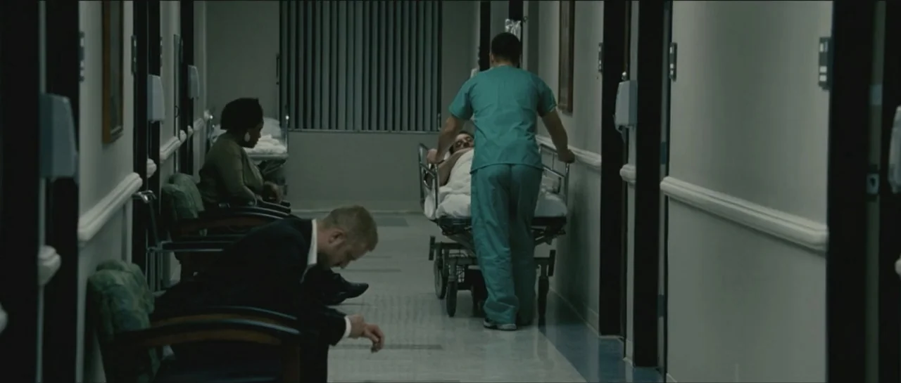 Contraband (2012) movie still: medium — A long hospital corridor with white walls and dark door frames features waiting area seating. A medical…