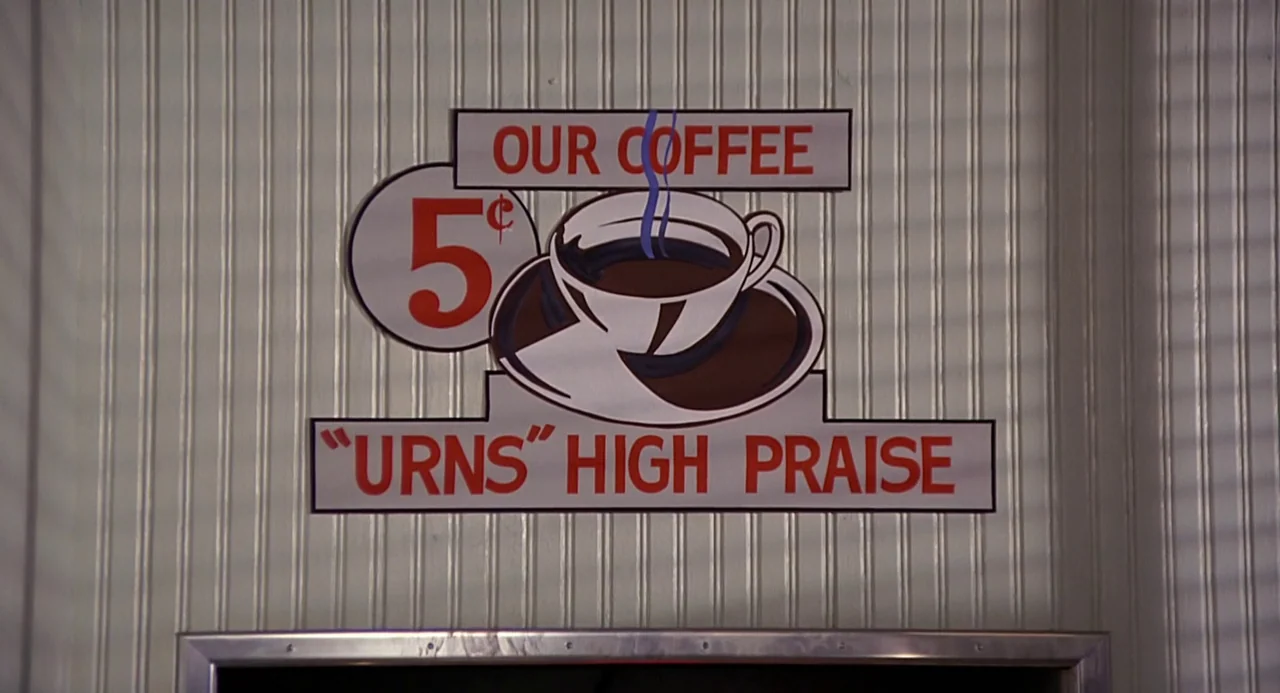 Back to the Future (1985) movie still: closeup — A flat painted sign is mounted on vertical white wood paneling in a diner. The sign depicts a…