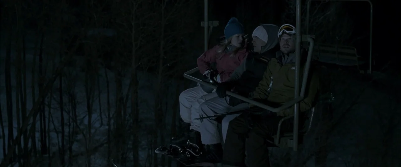 Frozen (2010) movie still: medium — A ski lift carries three people over dark snow-covered trees at night. The individuals sit closely together…