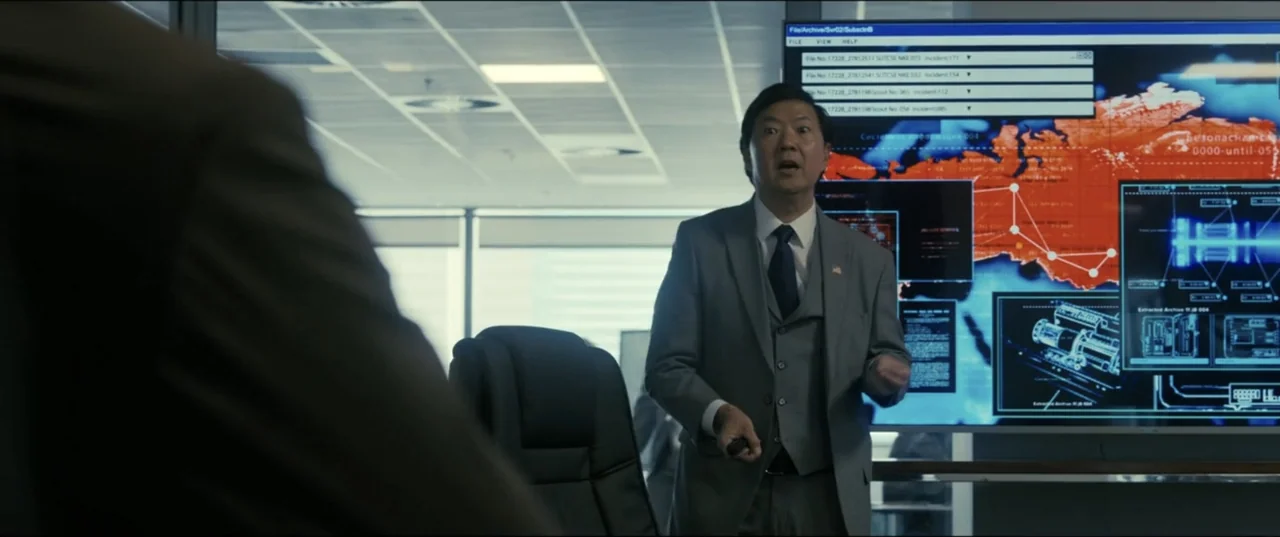 My Spy The Eternal City (2024) movie still: medium — A modern, minimalist glass-walled conference room features a large digital display showing…