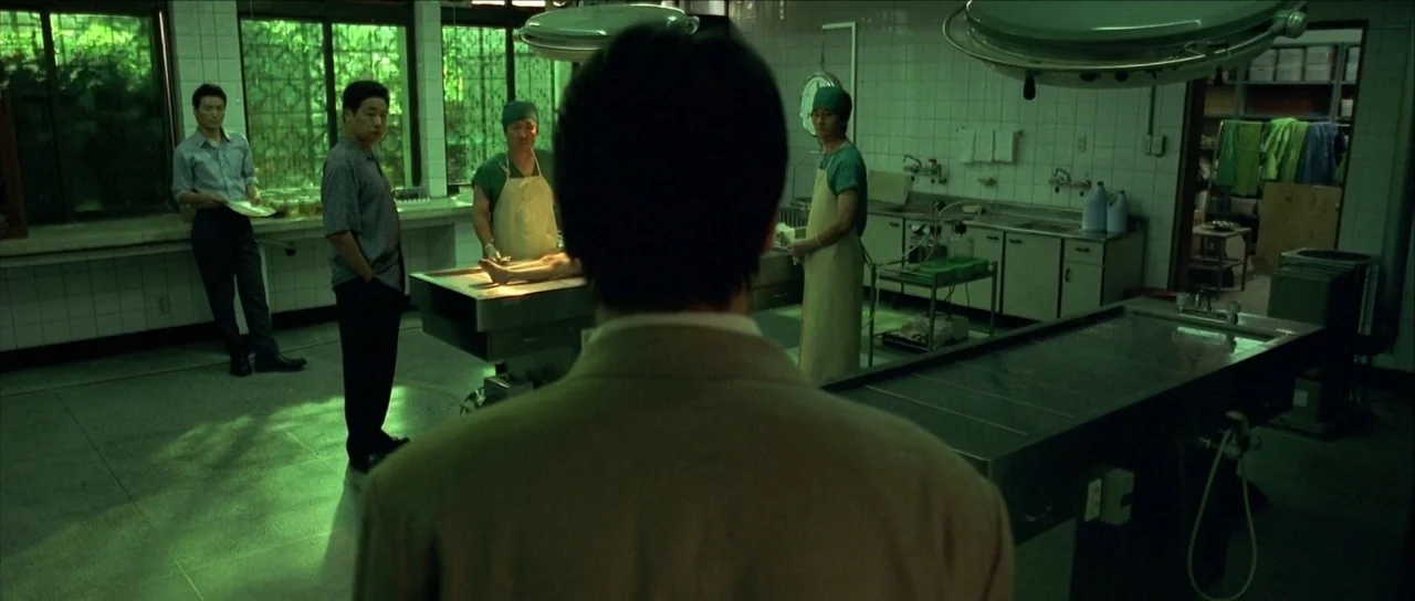Sympathy for Mr. Vengeance (2002) movie still: medium — A clinical morgue features tiled walls, metal autopsy tables, and large windows with grates.…