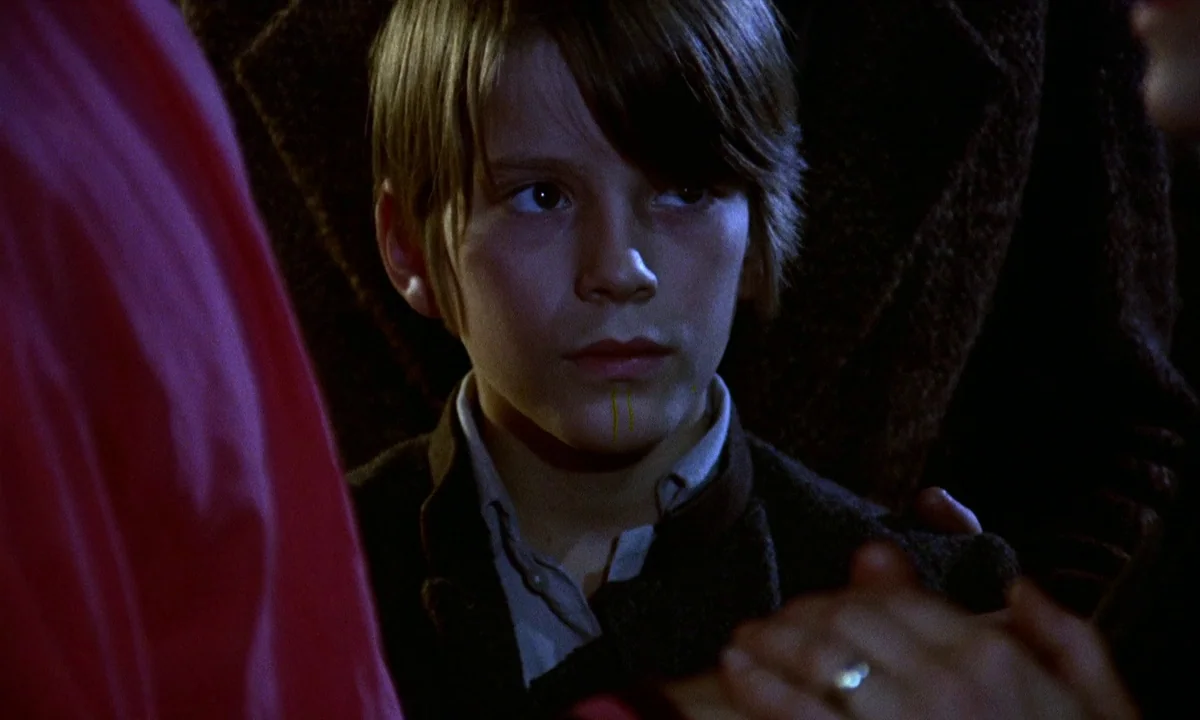 Vampire Circus (1972) movie still: closeup — A young boy stands in a dimly lit, shadowed environment. He looks toward the side while wearing a dark…