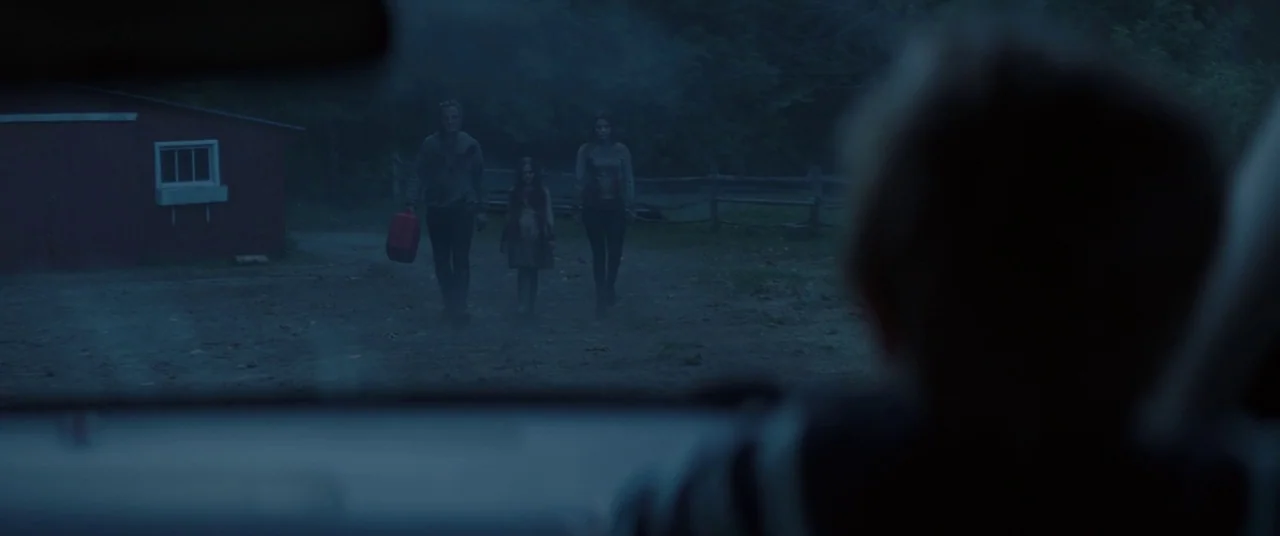 Pet Sematary (2019) movie still: wide — A rural dirt property at dusk featuring a red outbuilding and wooden fence. Three people approach the camera…