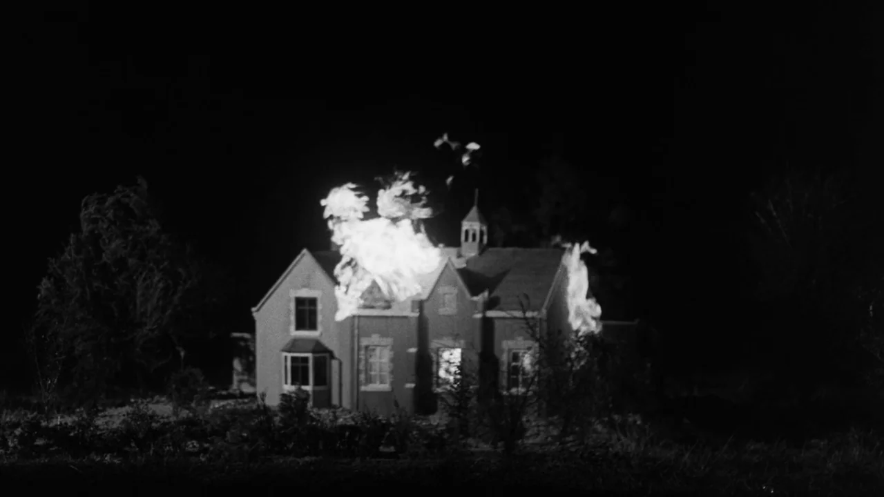 Village of the Damned (1960) movie still: wide — A miniature model of a house is set against a black background. Flames engulf the structure while…