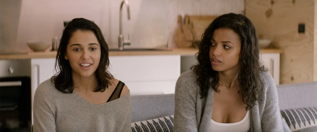 Charlie's Angels (2019) movie still: medium — A modern domestic space with a blurred kitchenette visible in the background. Two young women in grey…