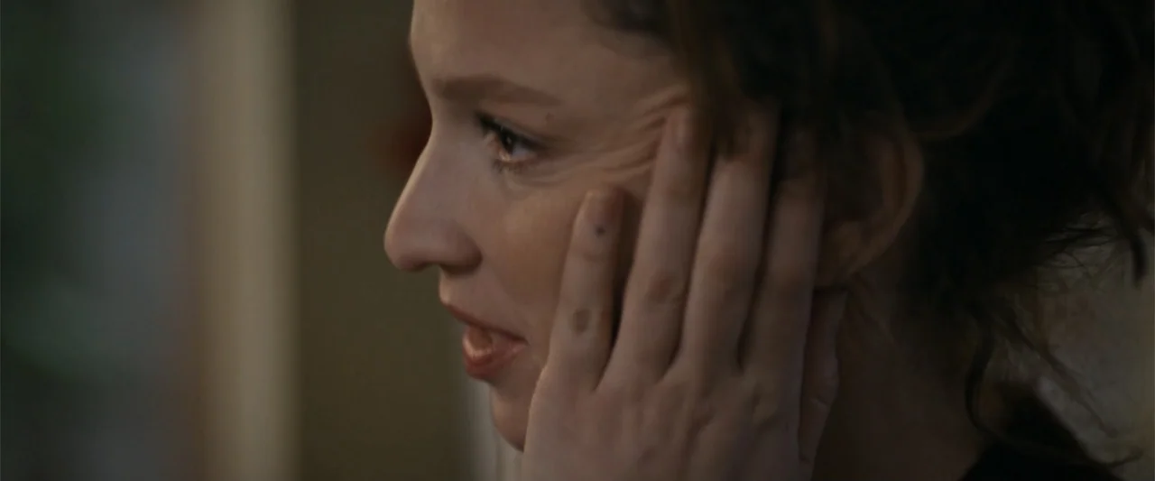 Silent Night, Deadly Night (2025) movie still: closeup — A dimly lit indoor space with blurred background elements. A young woman in profile touches…
