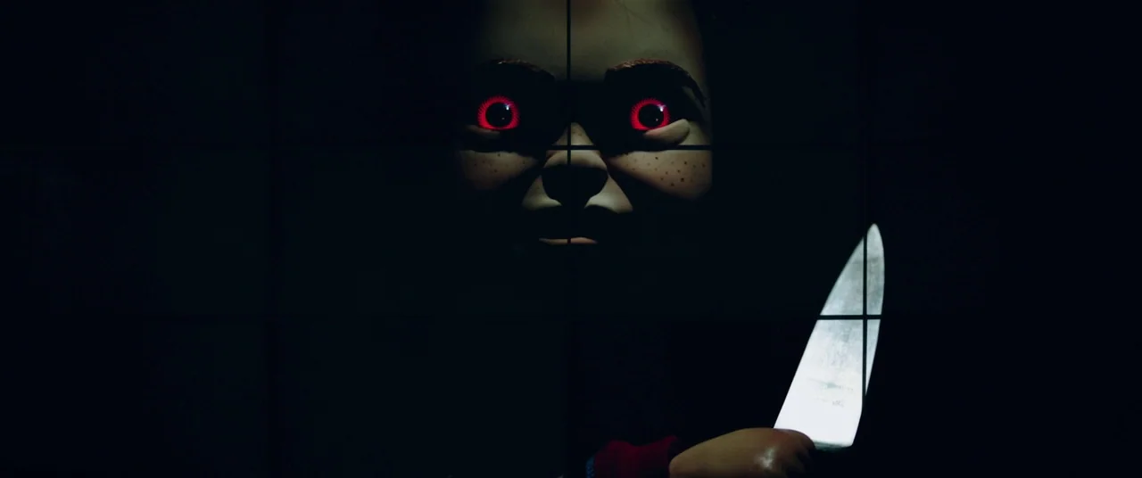 Child's Play (2019) movie still: closeup — A dark, obscured space contains only the face of a doll and a metallic blade. The doll's red eyes glow…
