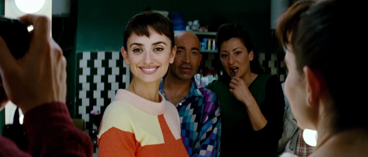 Broken Embraces (2009) movie still: medium — A well-lit room with green walls and checkered tile patterns on the back wall. Three adults pose for a…