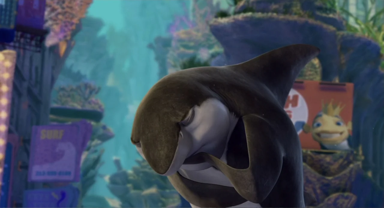Shark Tale (2004) movie still: medium — An animated orca poses in an underwater urban environment filled with coral structures. A small fish with a…