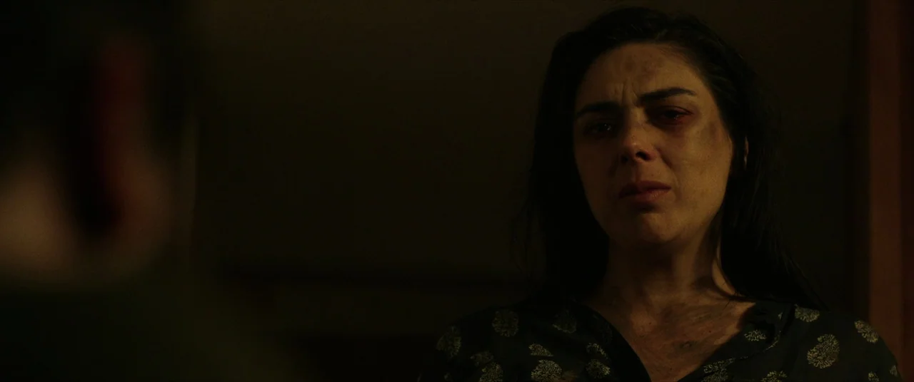Terrified (2017) movie still: closeup — A dimly lit room with heavy shadows obscures the surrounding details. A woman stands in the mid-ground…