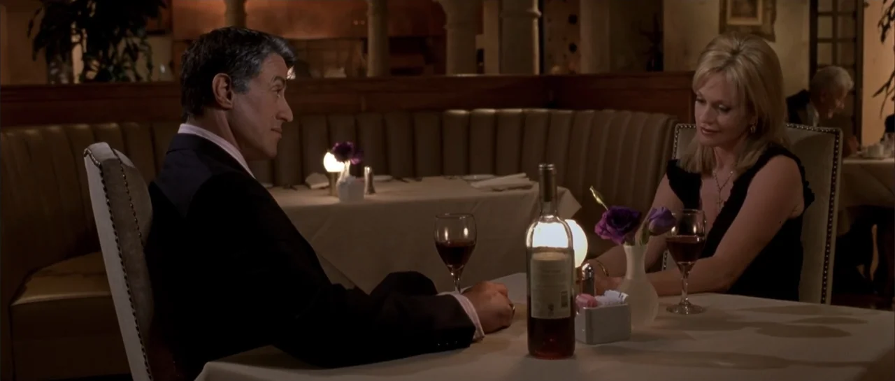 Shade (2003) movie still: medium — An upscale dining space with cream-colored booths and white tablecloths at night. A man in a suit and a blonde…
