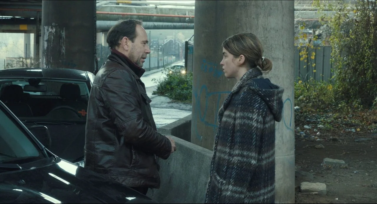 The Unknown Girl (2016) movie still: medium — An urban space beneath a highway overpass features weathered concrete supports and blurred road…