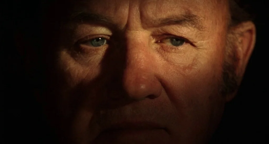 The Quick and the Dead (1995) movie still: closeup — An elderly man's face is illuminated in a dark, indistinct environment. The lighting draws…