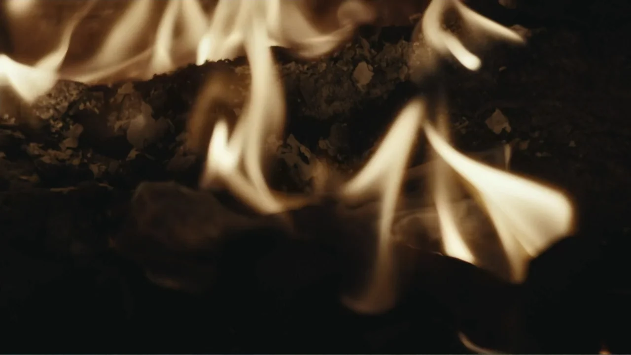 Demon in the White House (2021) movie still: closeup — An intense fire burns with bright yellow flames dancing over dark, smoldering embers.…