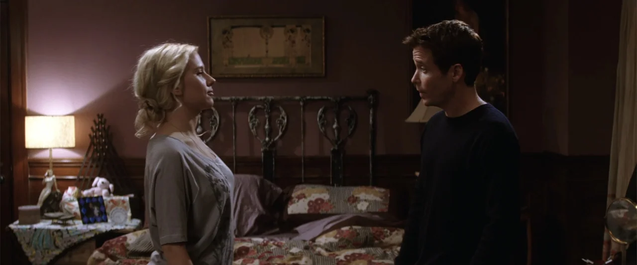 He's Just Not That Into You (2009) movie still: medium — A dimly lit bedroom features floral bedding and an ornate dark wood headboard. A man and a…