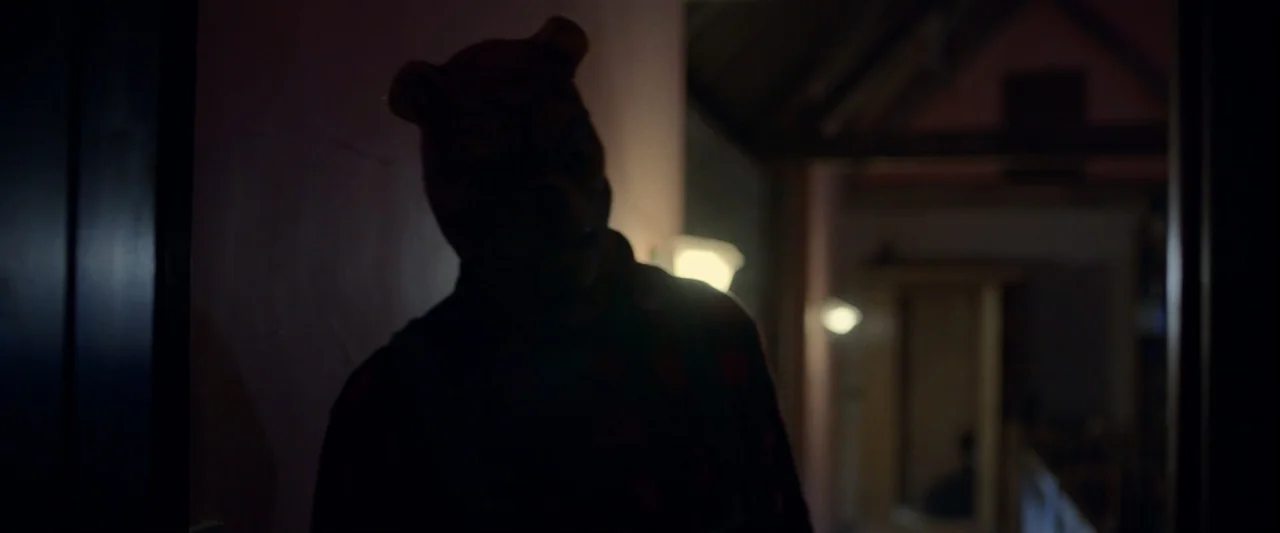 Winnie-the-Pooh: Blood and Honey 2 (2024) movie still: medium — A dark, dimly lit domestic hallway is seen at night. A person wearing an animal mask…