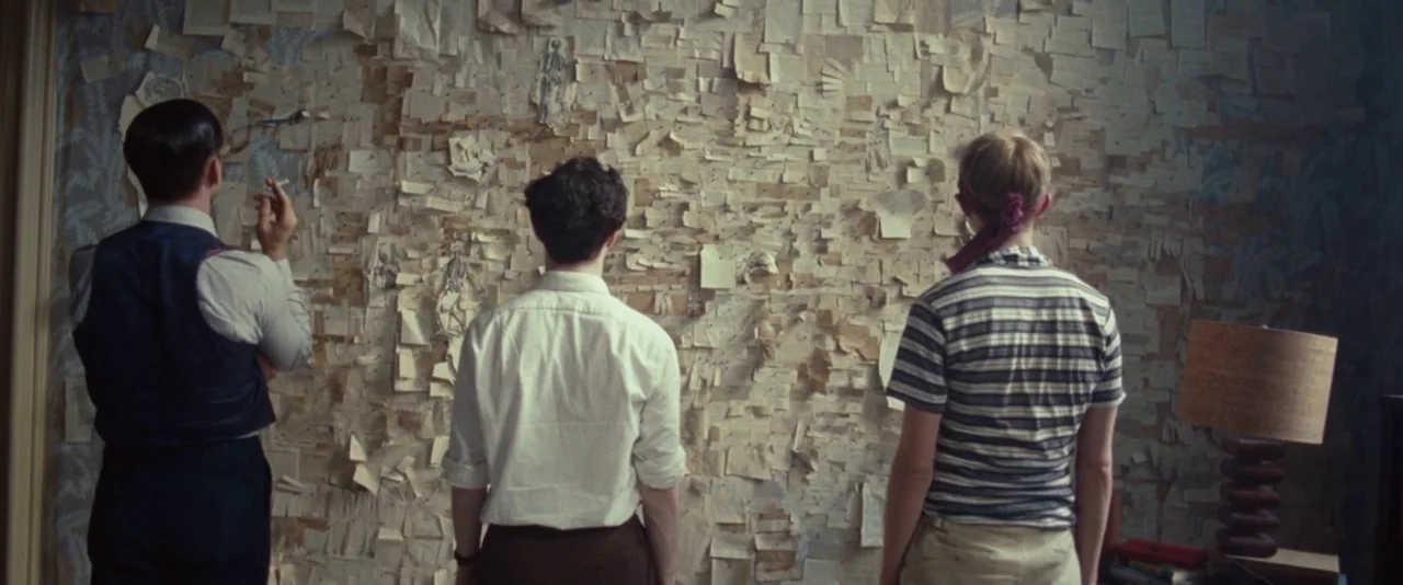 Kill Your Darlings (2013) movie still: medium — A room features a large wall entirely covered in pinned notes and sketches. Three men stand together…