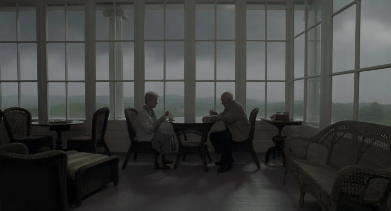The Green Mile (1999) movie still: wide — A glass-enclosed sunroom with wicker furniture sits under a dark, cloudy sky. An elderly man and woman are…