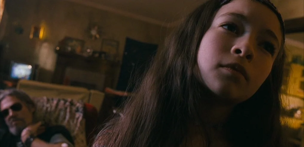 Tideland (2005) movie still: closeup — A dimly lit room contains a young girl and a resting elderly man. The girl looks upward while the man sits in…