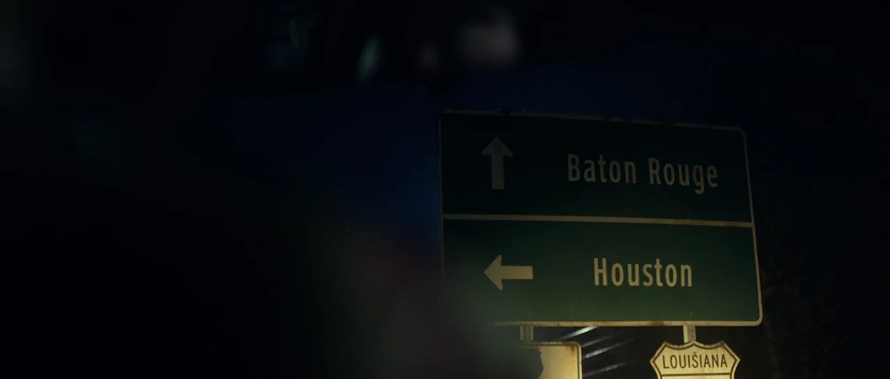 10 Cloverfield Lane (2016) movie still: medium — A dark night scene displays a green road sign with white text directions. The sign directs traffic…