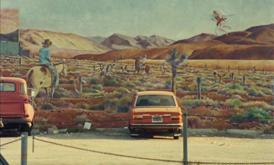 Documenteur (1981) movie still: wide — A paved asphalt area fronts a large desert-themed mural painted on a vertical surface. The mural depicts a…