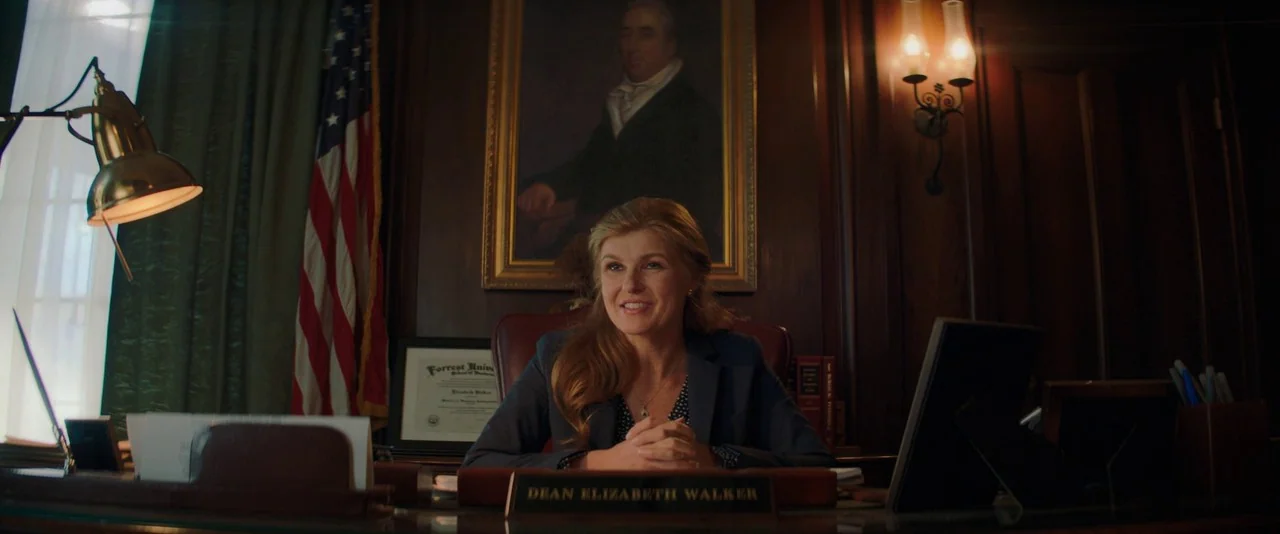 Promising Young Woman (2020) movie still: medium — A dark-paneled university office featuring an American flag and a framed portrait behind a desk.…