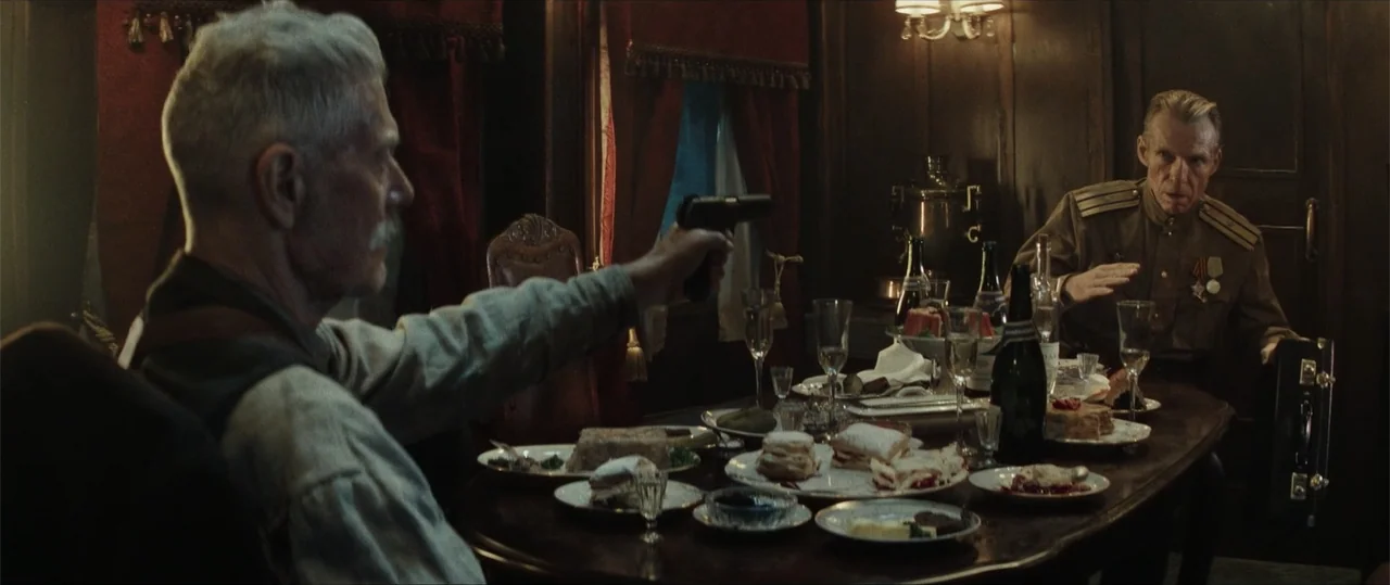 Sisu: Road to Revenge (2025) movie still: medium — A dimly lit dining car features wood-paneled walls and a table full of plates. An older man aims…
