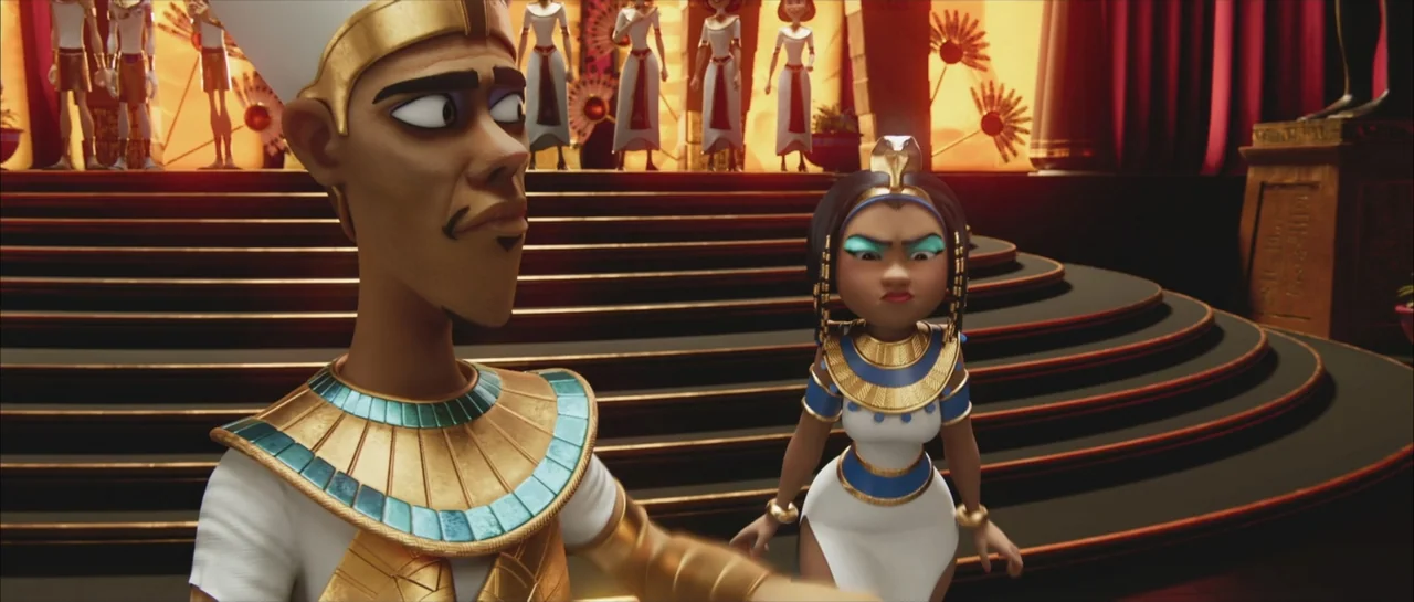 Mummies (2023) movie still: medium — An interior Egyptian palace space with tiered flooring and dark red drapery. A man in royal attire stands…