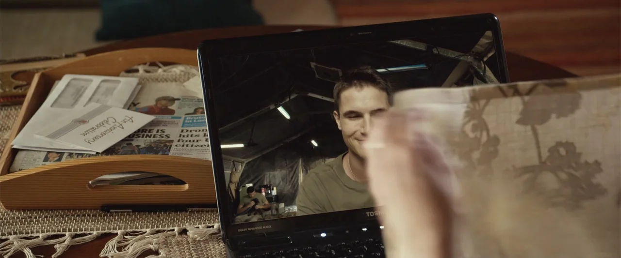Max (2002) movie still: medium — A laptop screen rests on a wooden coffee table near an open newspaper. A man is visible on the video chat screen…
