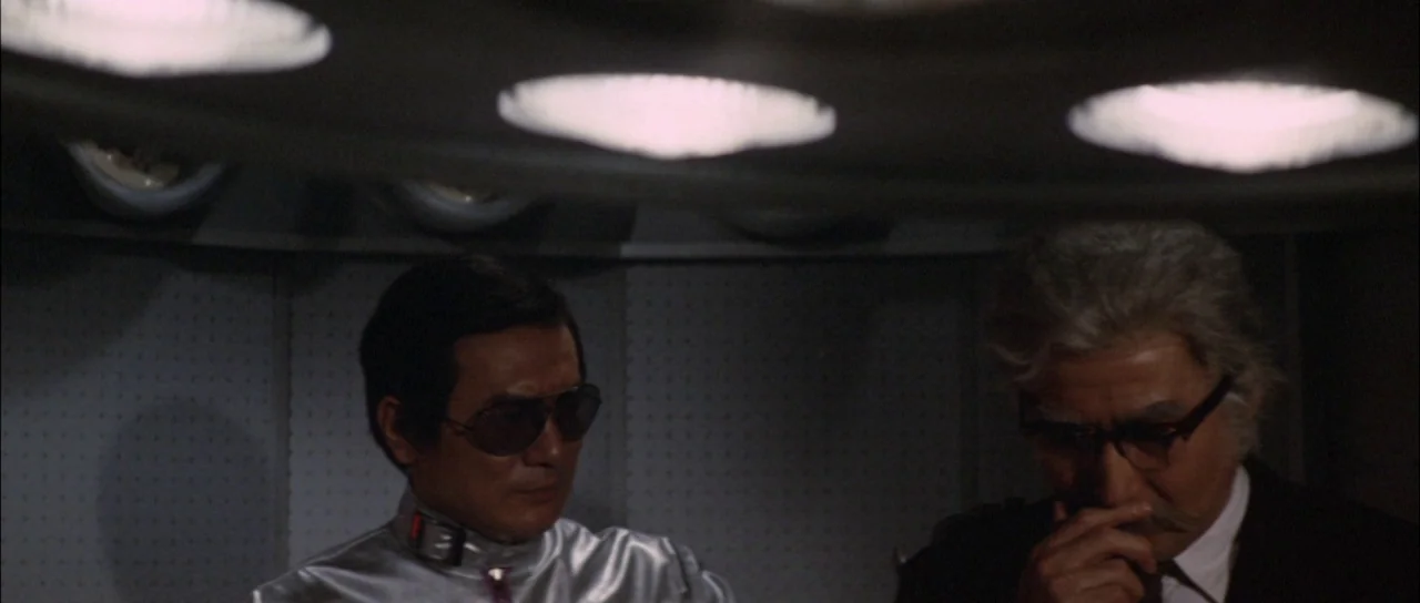 Terror of Mechagodzilla (1975) movie still: medium — A dimly lit indoor space features metallic wall textures and overhead circular lighting…