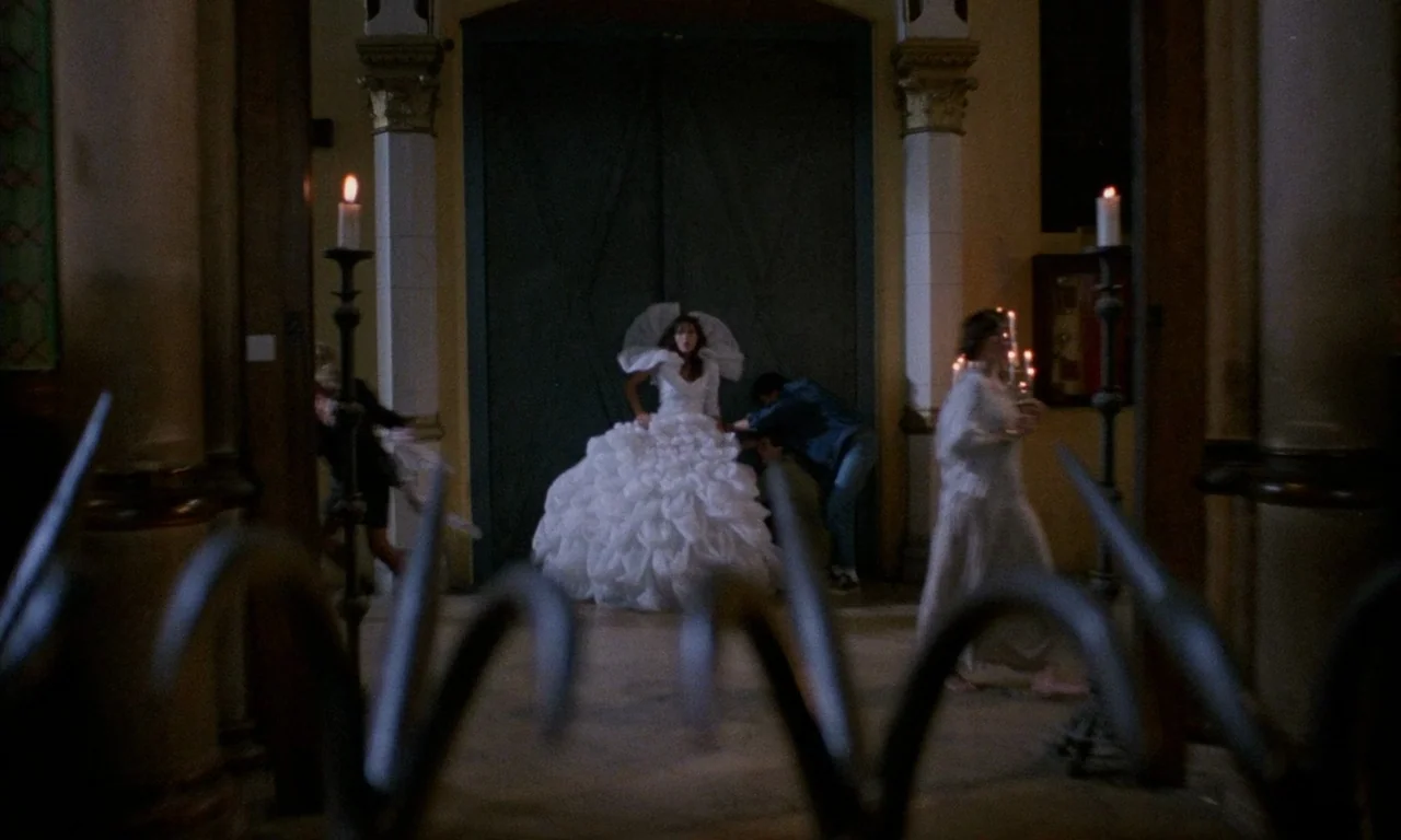 The Church (1989) movie still: wide — The interior of a dimly lit church features tall stone pillars and a central door. A woman in a large white…